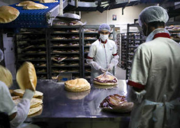 Employees, wearing personal protective equipment, pack bread at a bakery in the Lebanese capital Beirut on March 30, 2020. - Lebanon has reported 446 COVID-19 cases to date, with 11 deaths. To try to contain the spread of the virus, Lebanon has imposed isolation measures on its population until April 12, with a nighttime curfew in effect. Schools, universities, restaurants and bars are closed. (Photo by PATRICK BAZ / AFP)