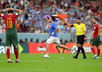 A man wearing a t-shirt reading "Save Ukraine" and "Respect For Iranian Woman" runs on the pitch waving a rainbow flag on the pitch during the Qatar 2022 World Cup Group H football match between Portugal and Uruguay at the Lusail Stadium in Lusail, north of Doha on November 28, 2022. (Photo by PATRICIA DE MELO MOREIRA / AFP)