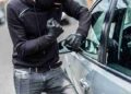 The man dressed in black with a balaclava on his head trying to break into the car. He uses a screwdriver. Car thief, car theft concept