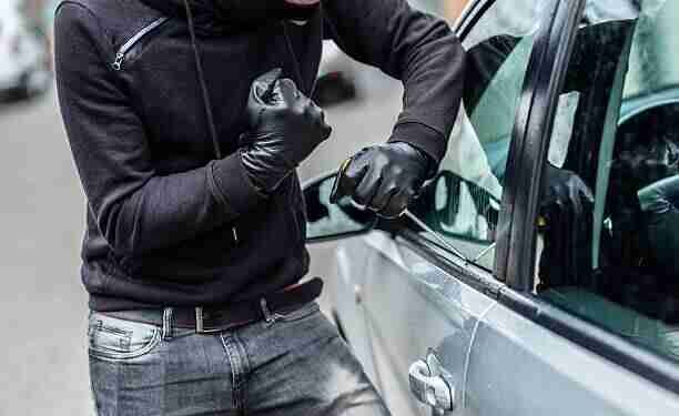 The man dressed in black with a balaclava on his head trying to break into the car. He uses a screwdriver. Car thief, car theft concept