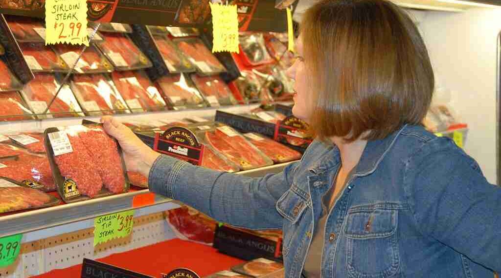 B0DDTX A woman selects meat while grocery shopping.. Image shot 2008. Exact date unknown.