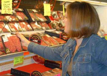 B0DDTX A woman selects meat while grocery shopping.. Image shot 2008. Exact date unknown.