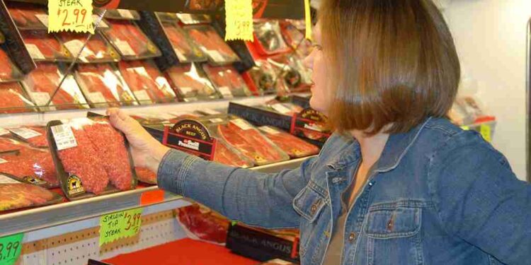 B0DDTX A woman selects meat while grocery shopping.. Image shot 2008. Exact date unknown.